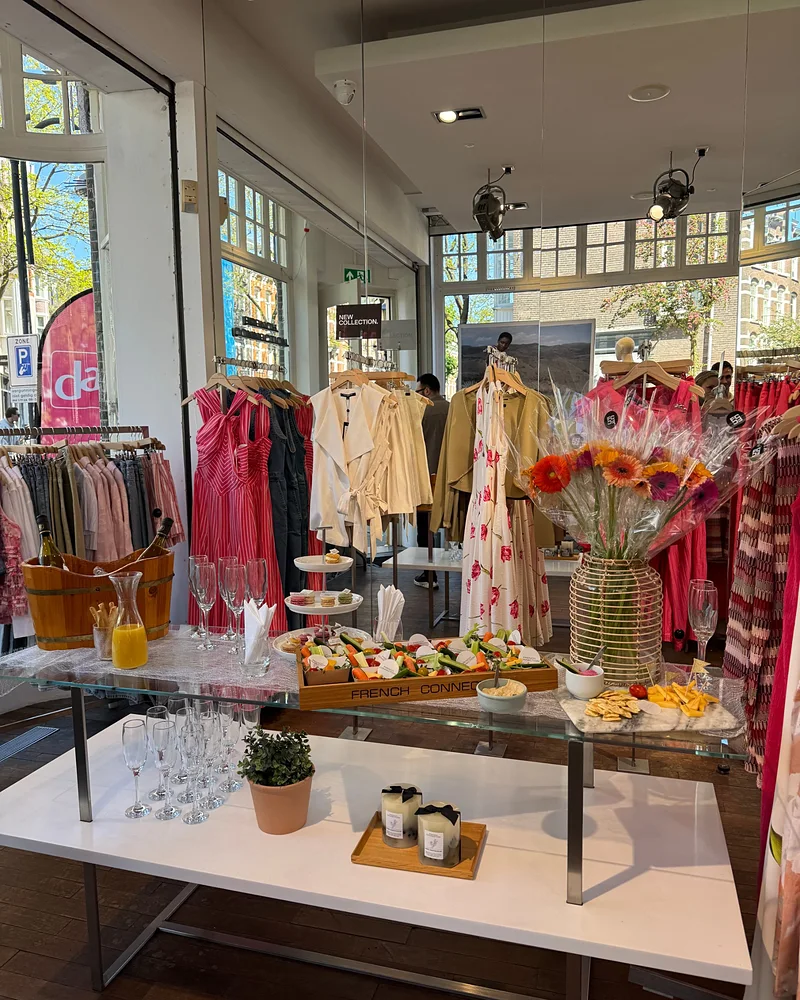 The event table at French Connection Amsterdam with drinks, macarons and flowers in front of the SS26 collection