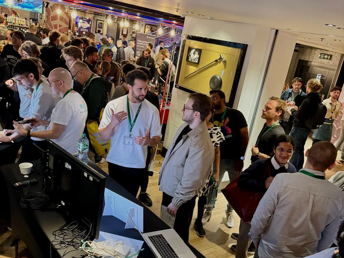 A StyleAI co-founder talking with a visitor at the StyleAI demo table, in a crowded room of booths at the AI Agents World Tour in London